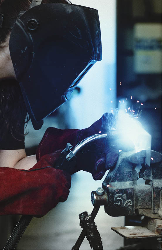 Female welding a metal piece in the garage