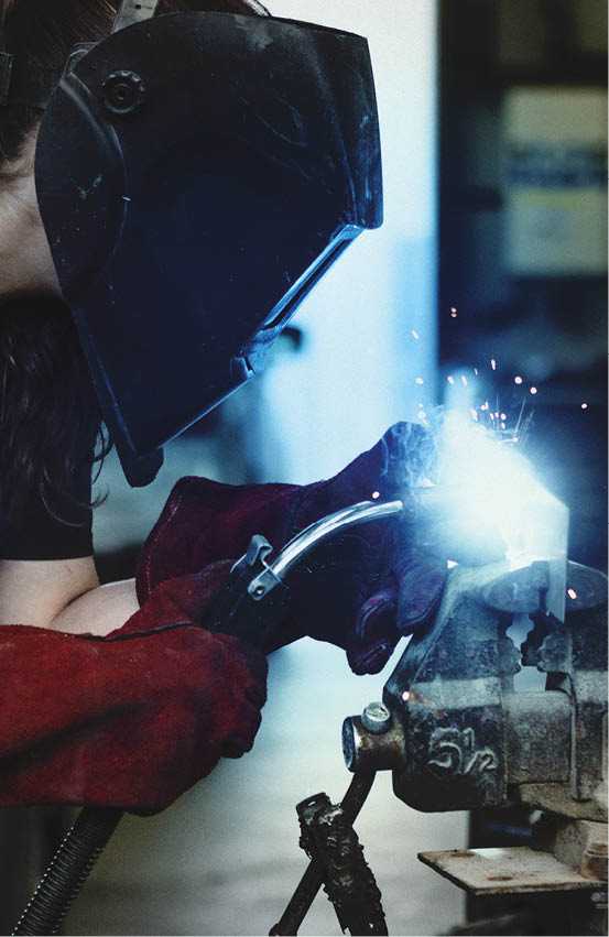Female welding a metal piece in the garage