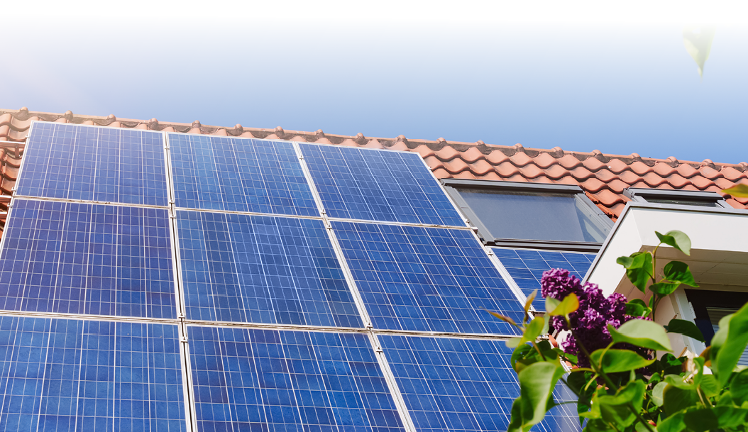 Solar panel on a red roof reflecting the sun and the cloudless blue sky.