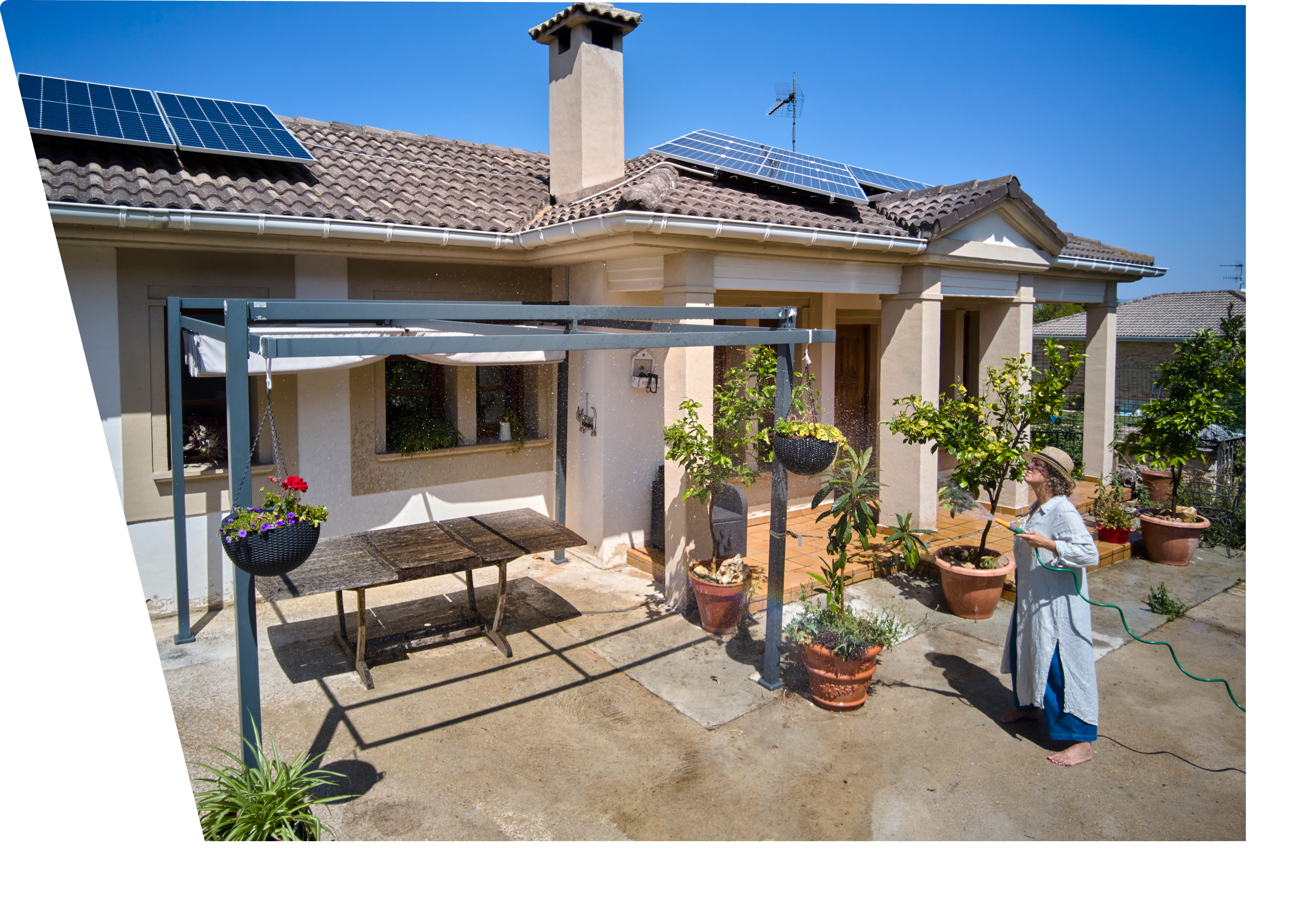 A woman is watering plants in a sunny backyard that features solar panels on the roof. The scene captures a moment of care and sustainability, set in an eco-friendly environment with lush greenery and a warm atmosphere.