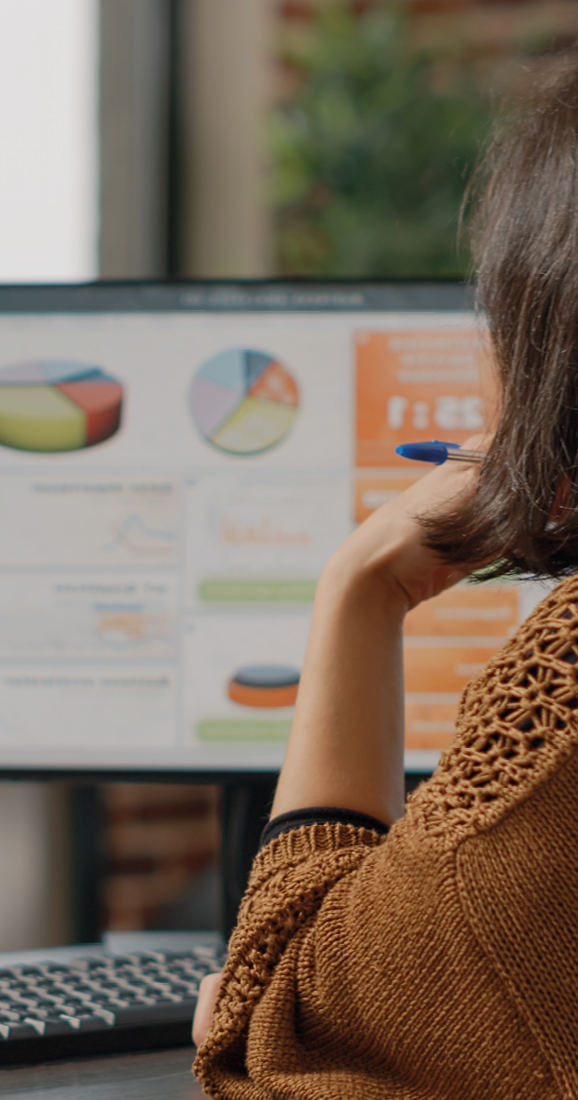 Business woman analyzing rate charts on computer and files to plan project and strategy. Employee using information on monitor and documents to design marketing presentation at desk.