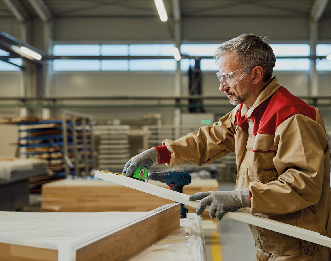 Woodworker checking measurements of a plank while working at carpentry workshop.
