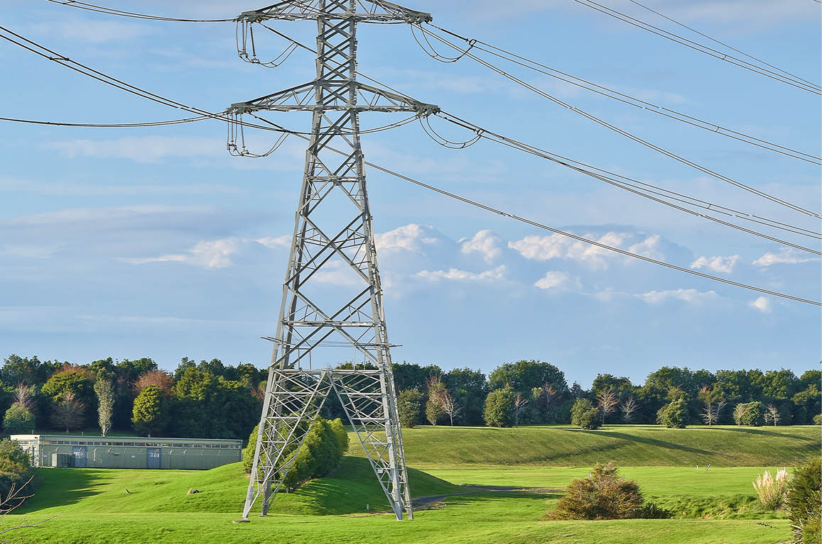 A vertical shot of high voltage electric tower with green meadow in the foreground